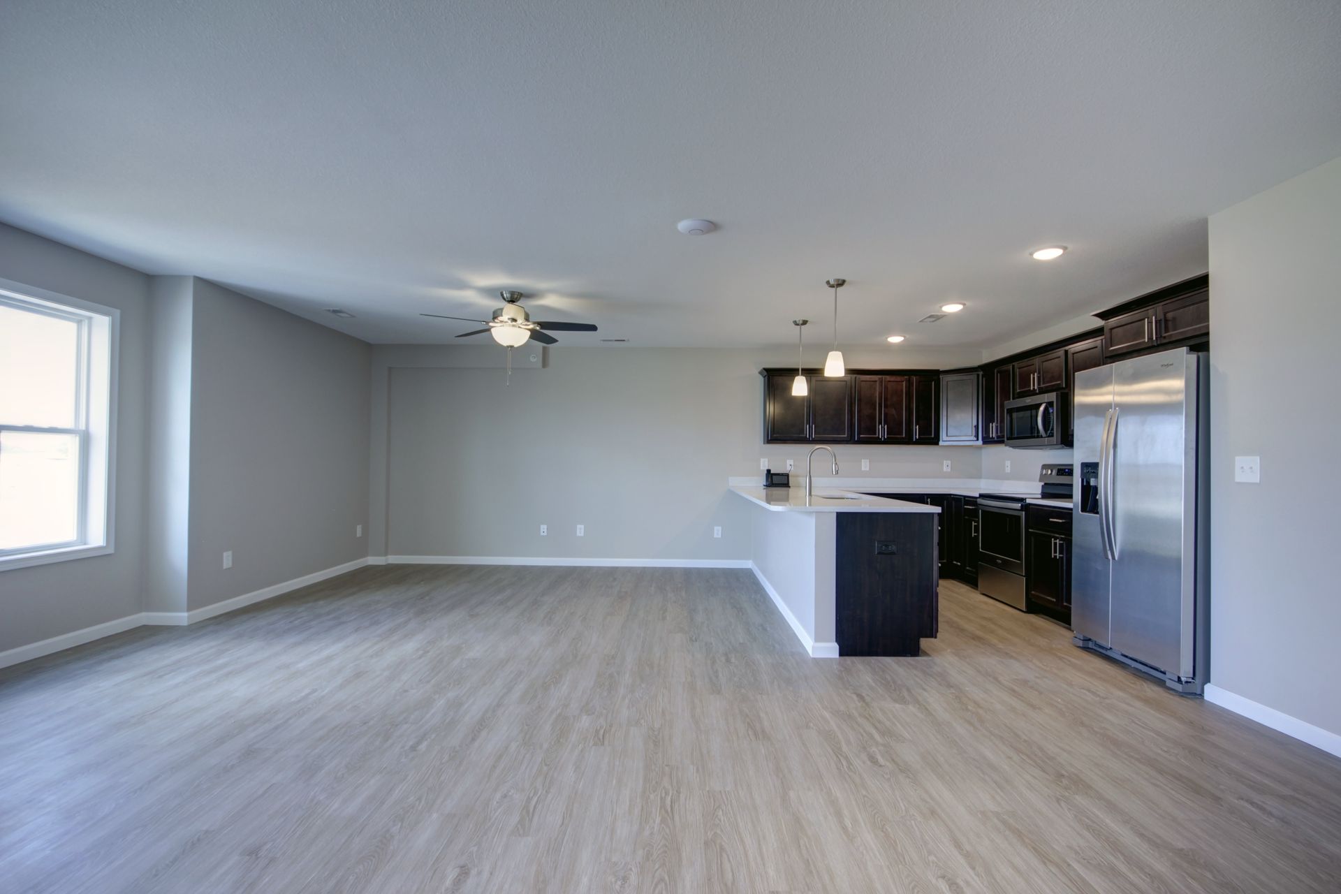 Empty open-concept living room and kitchen with gray walls, light wood floors, and stainless steel appliances
