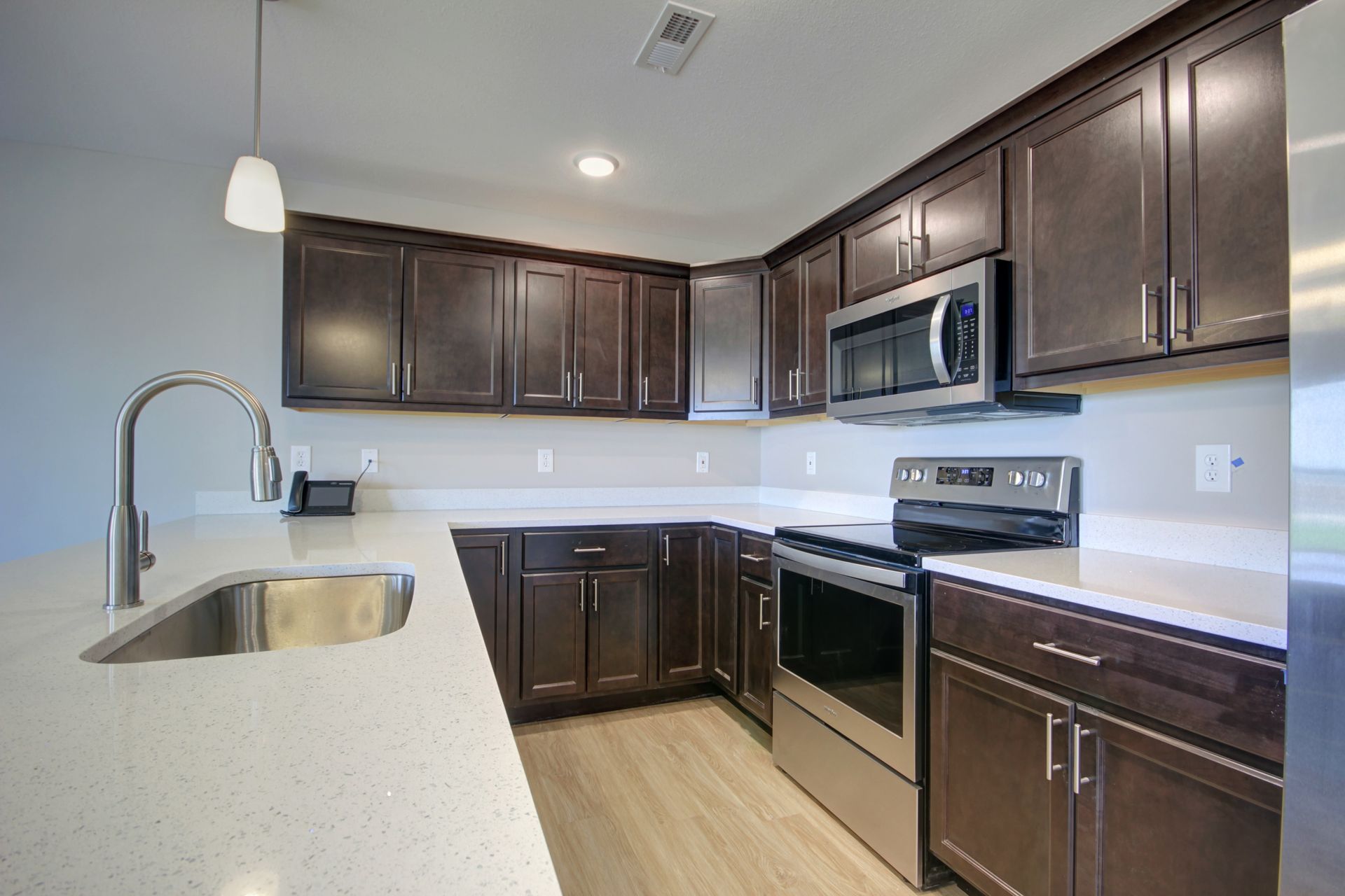Modern kitchen with dark wood cabinets, white countertops, stainless steel appliances, and a sink island.
