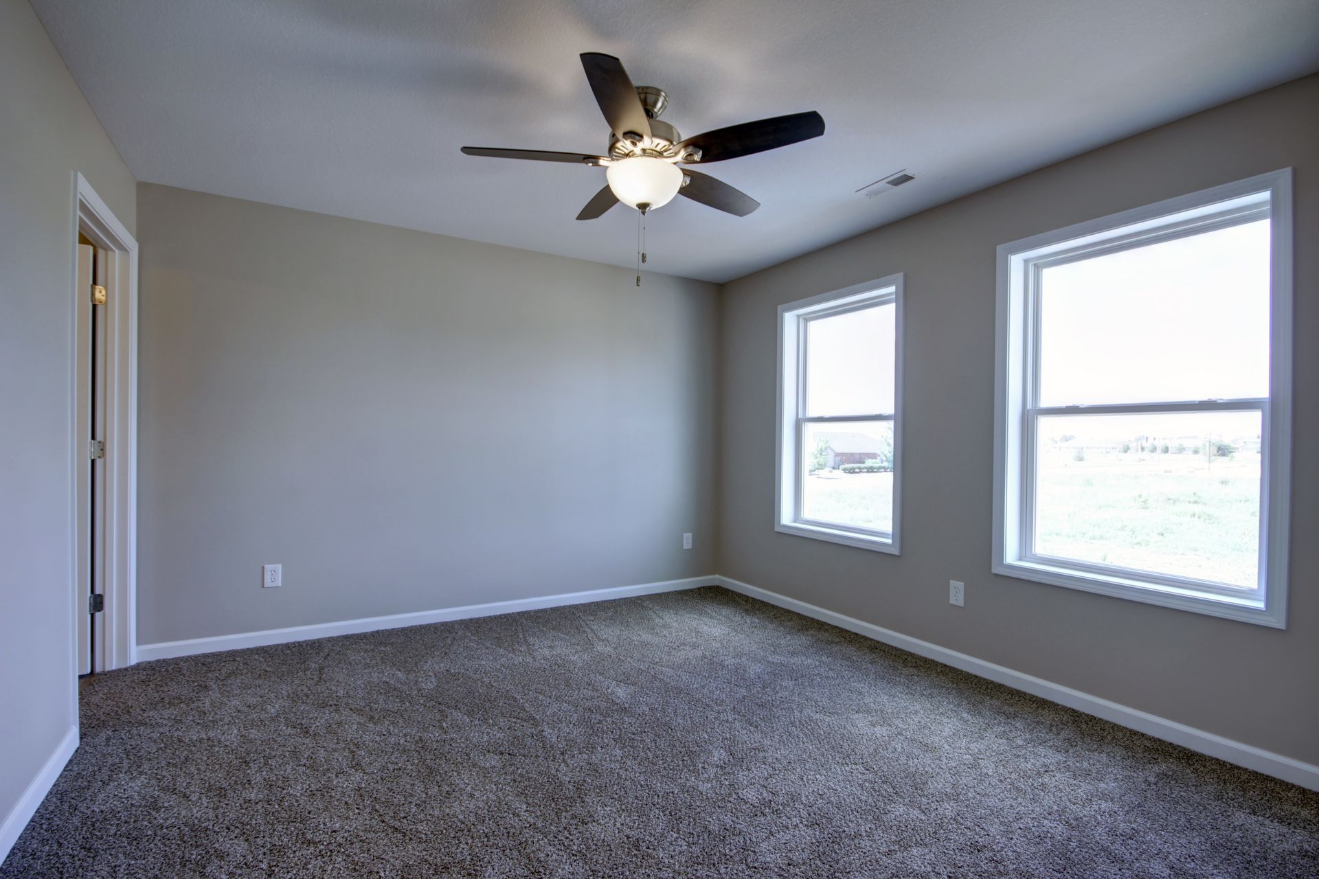 Empty gray bedroom with carpet, ceiling fan, and two windows.