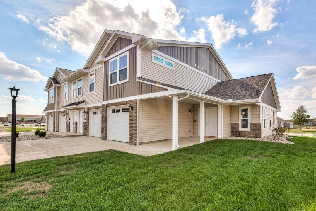 Modern beige townhouse with attached garages and green lawn under a partly cloudy sky