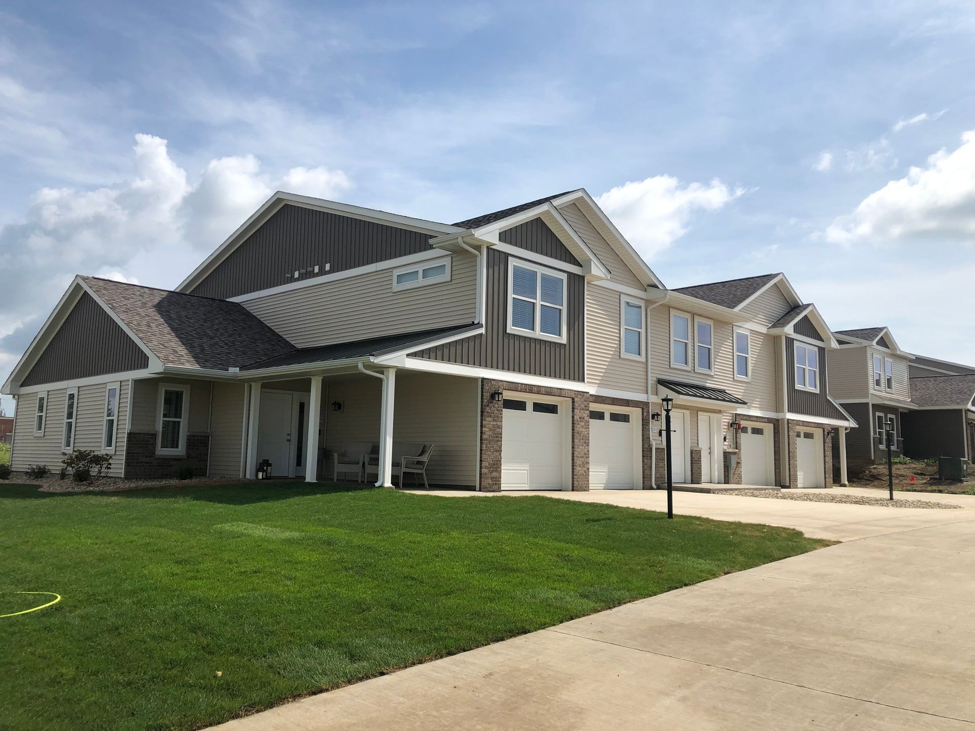 Row of modern suburban townhouses with garages, green lawn, and a concrete driveway under a cloudy sky