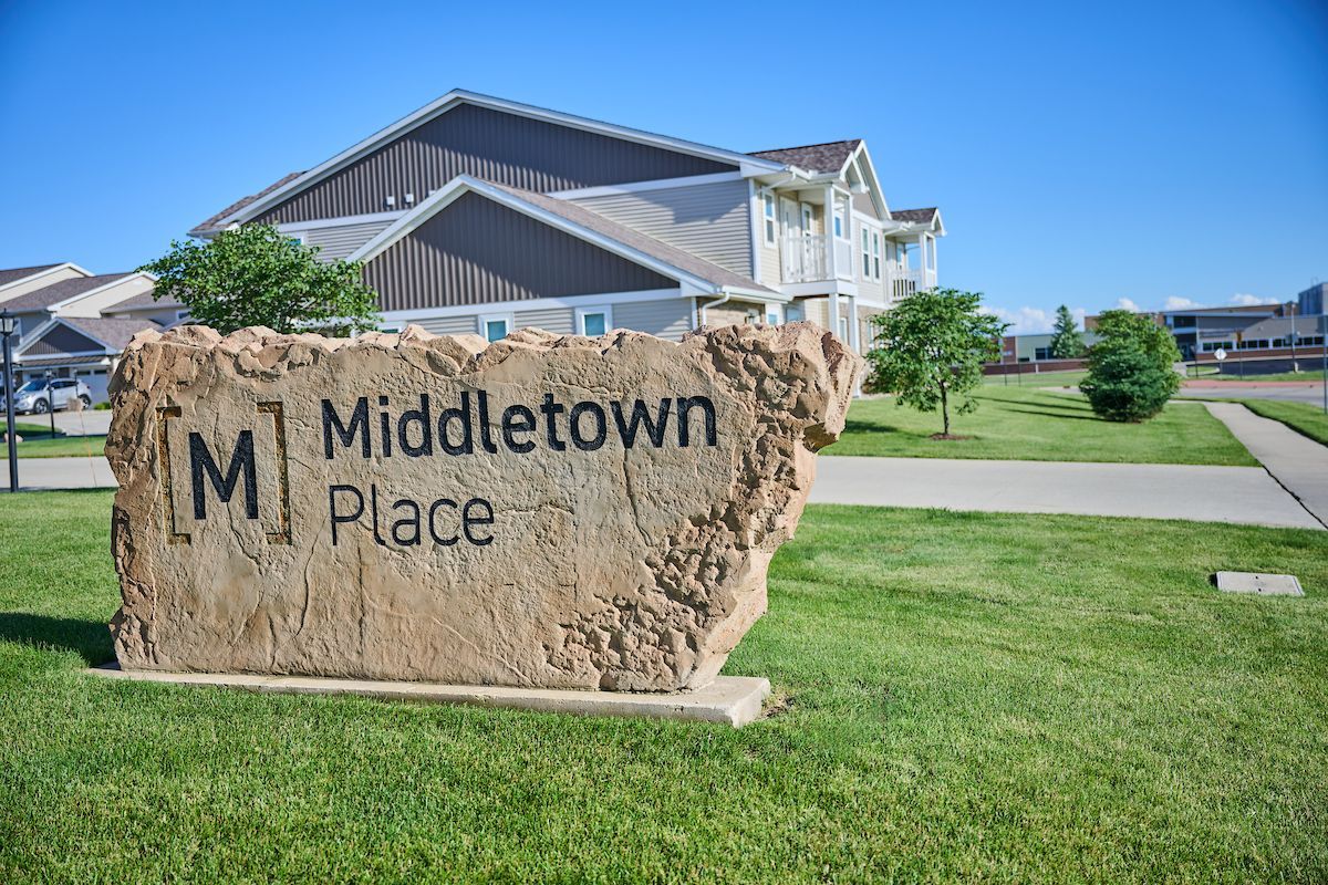 Stone sign reading “Middletown Place” in front of apartment buildings and green lawn under a blue sky
