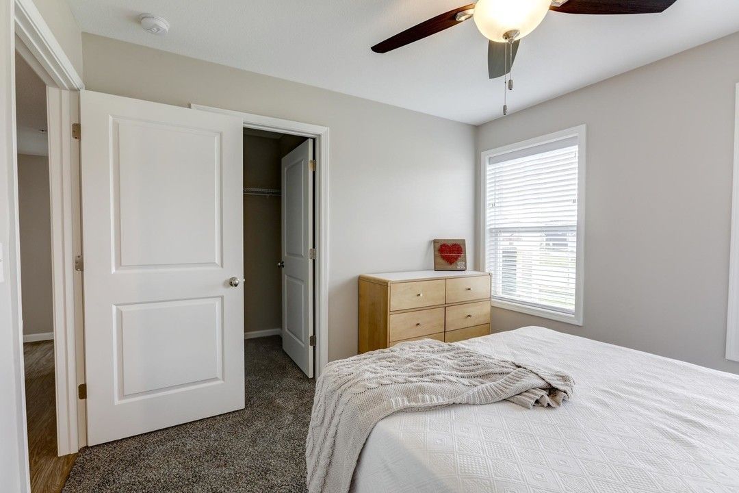 Bright bedroom with white bed, wooden dresser, open closet door, and ceiling fan