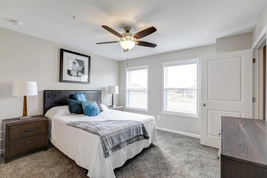 Bright bedroom with bed, nightstands, dresser, ceiling fan, and two windows