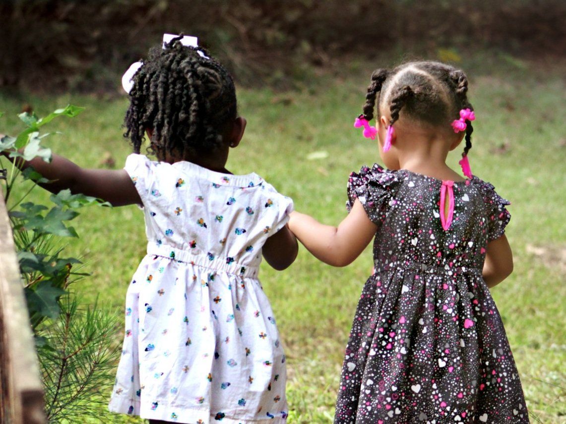 Two little girls are holding hands in the grass.
