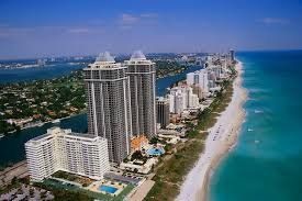 Aerial view of high-rise beachfront condos along a turquoise coastline under a clear blue sky