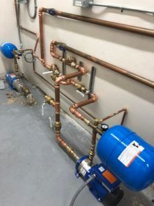 Copper pipes and blue pressure tanks along a basement wall with an exposed valve assembly