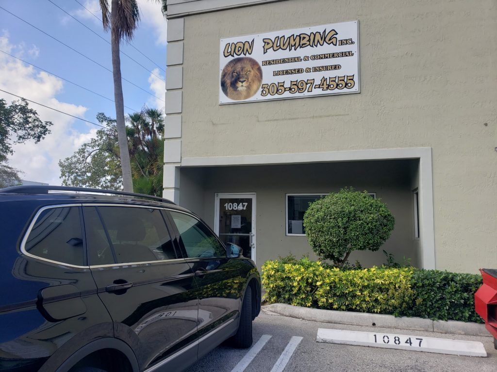 Black SUV parked beside a beige building with a storefront sign and small entrance.