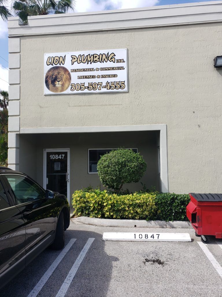 Dog grooming shop entrance with sign, parking spaces, and a red dumpster outside.