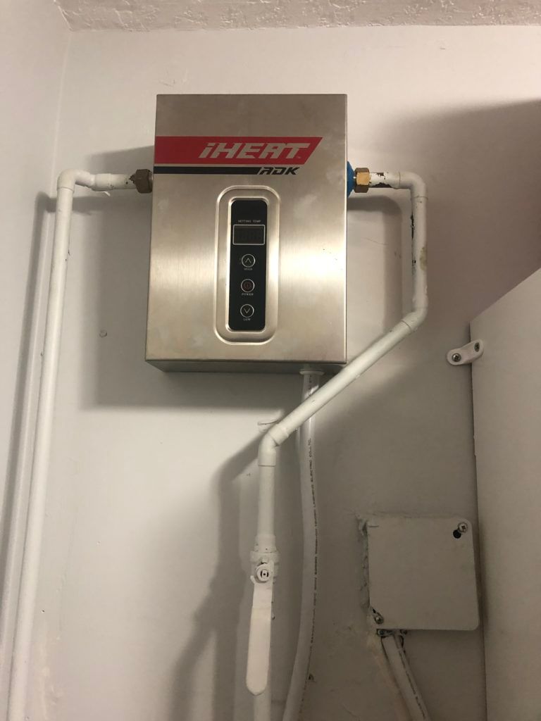 Wall-mounted HEAT unit with digital display and white pipes in a utility room