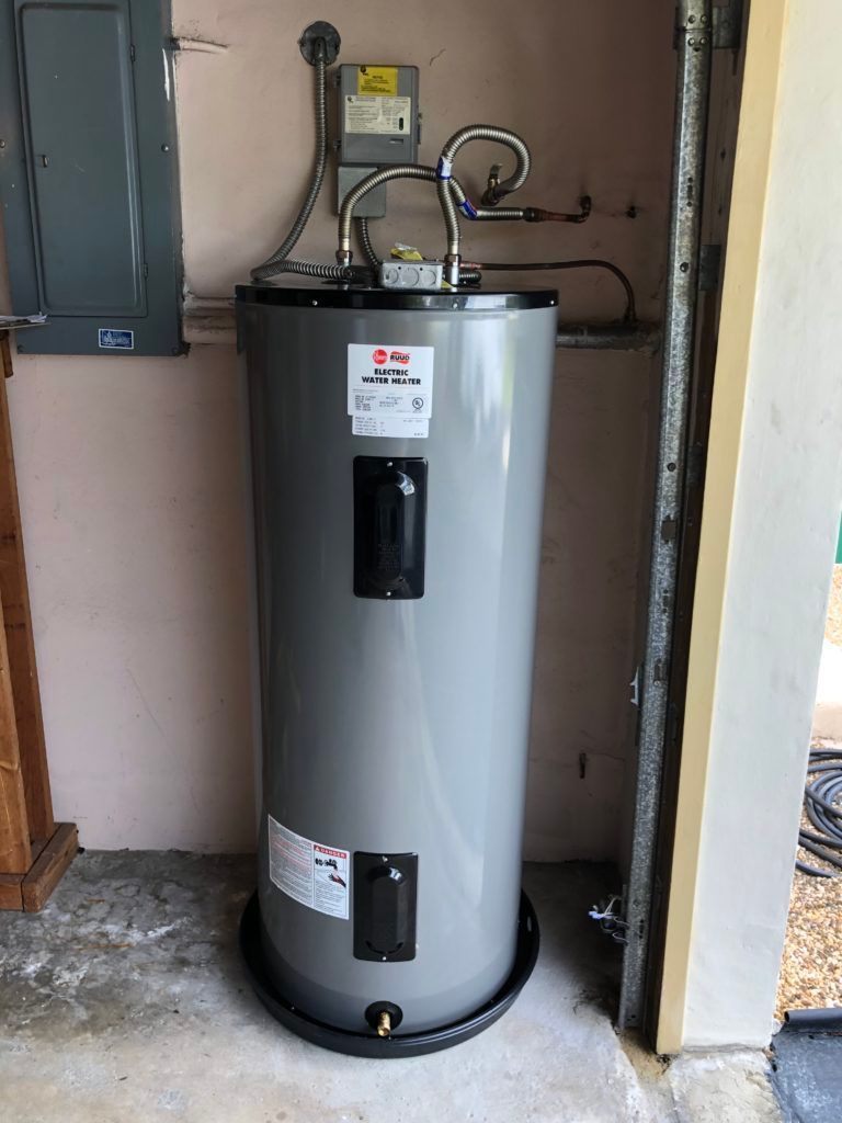 Gray water heater in a utility closet with pipes and a control panel.