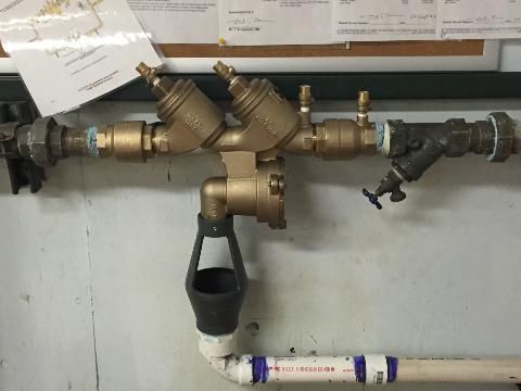 Brass pipe valve assembly with black fittings and a white PVC pipe in an industrial setting