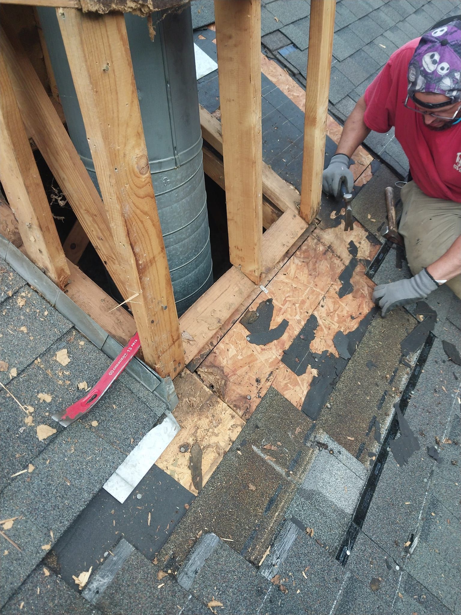 Man repairing roof near chimney. Damaged shingles, wooden frame, gray chimney visible.