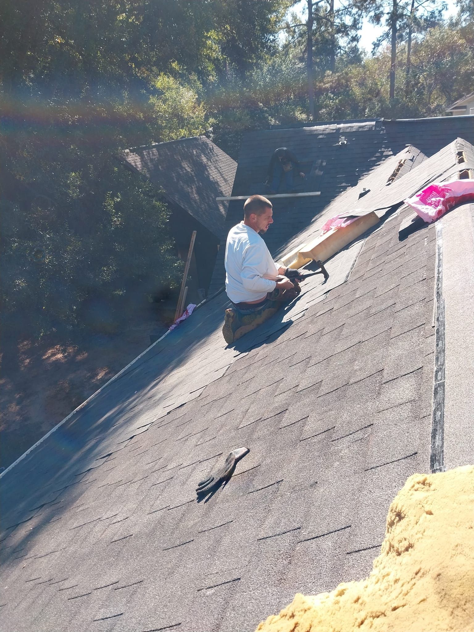 Person on a roof wearing white overalls and working with roofing materials in a sunny outdoor setting.