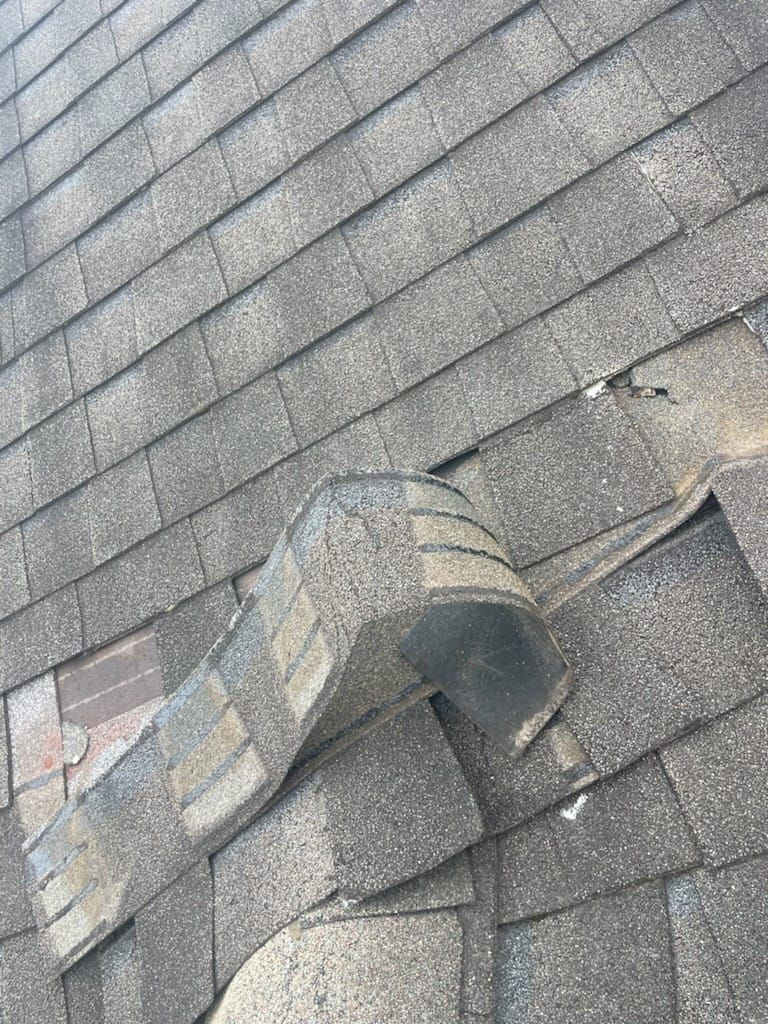 Damaged roof with curled and missing shingles, potentially exposing underlayment.