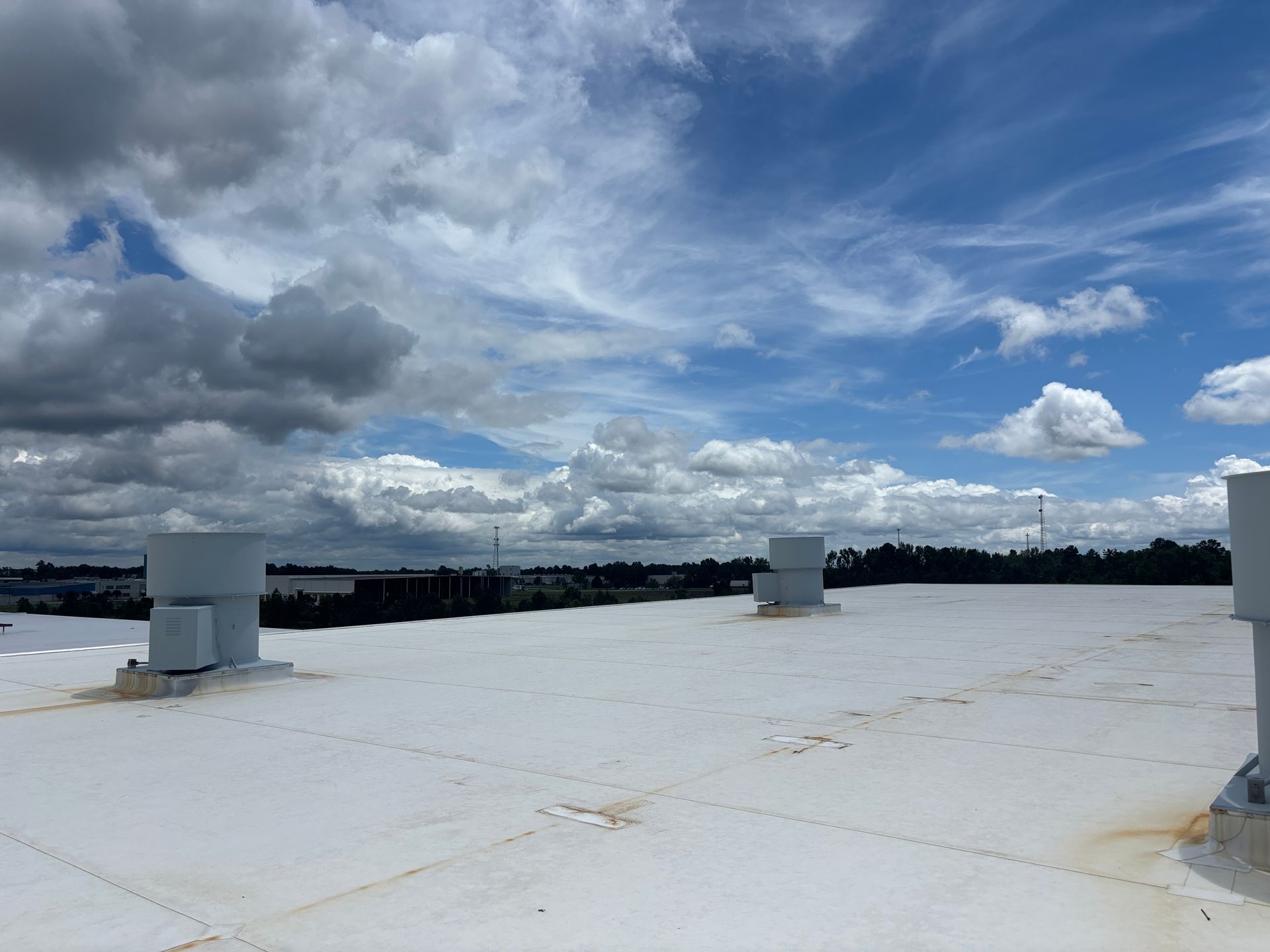 White roof with vents against a cloudy sky. Distant treeline.
