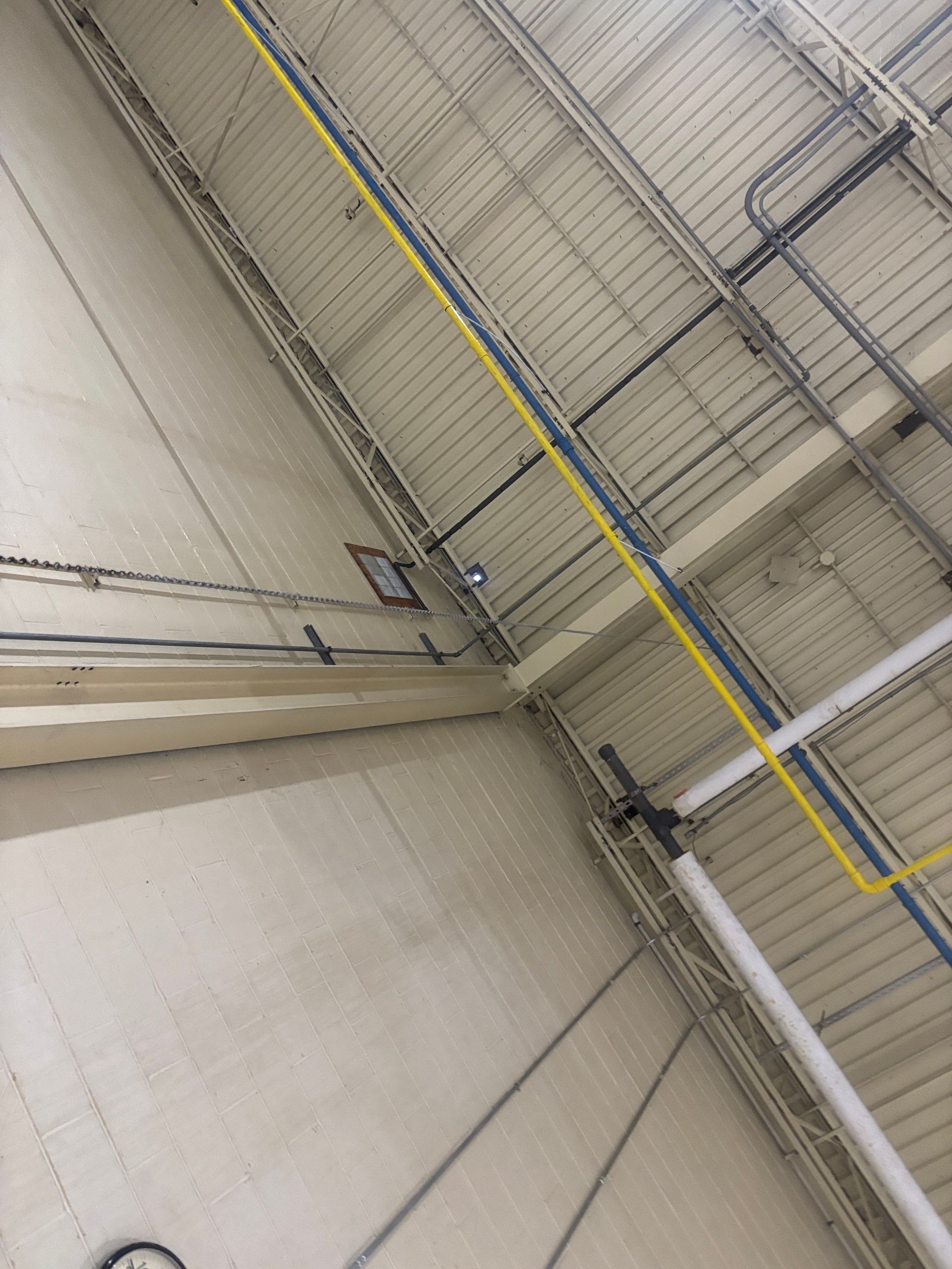Industrial interior ceiling with pipes and wiring; white walls.