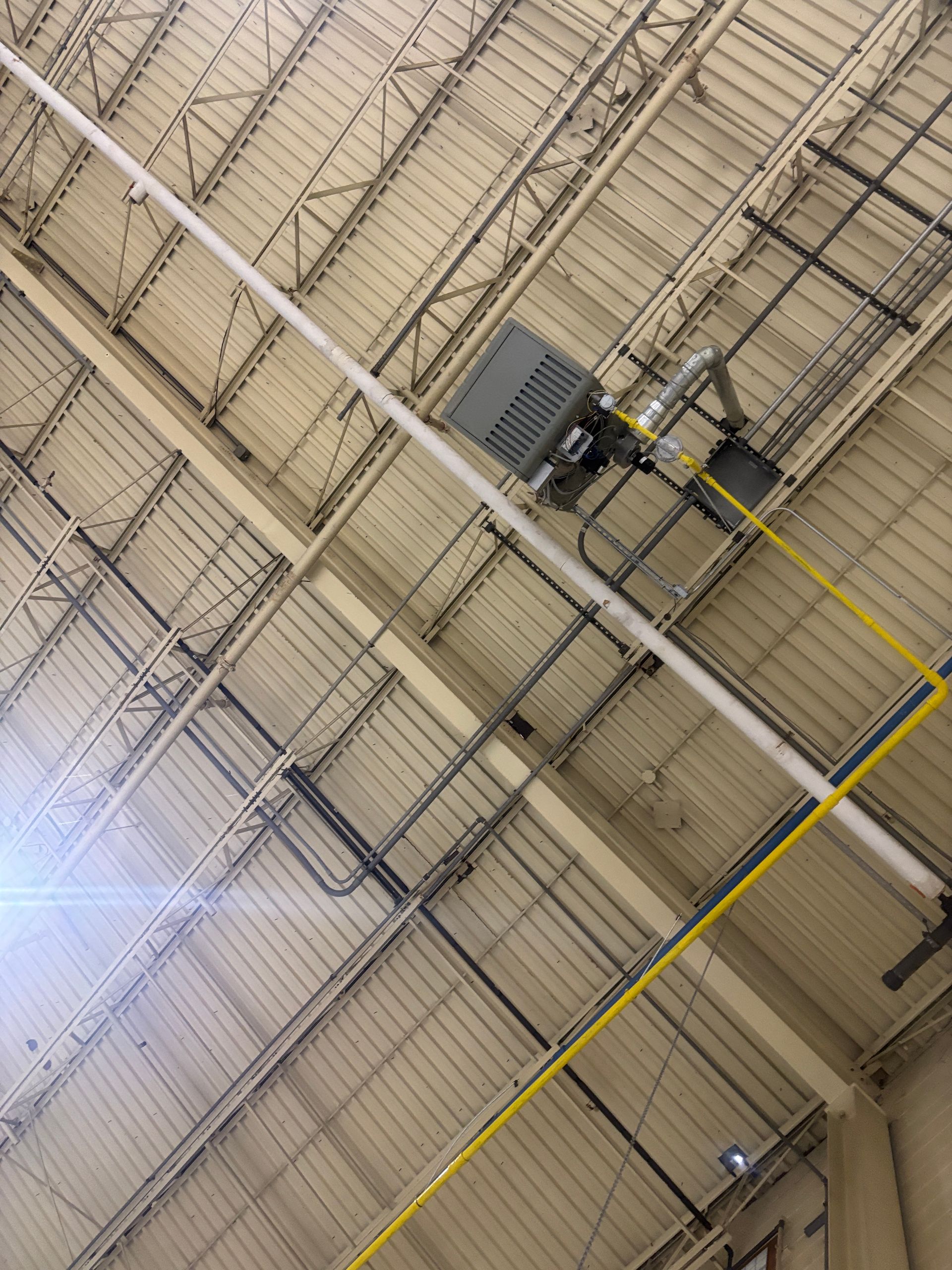 White industrial ceiling with metal beams, lights, and pipes.