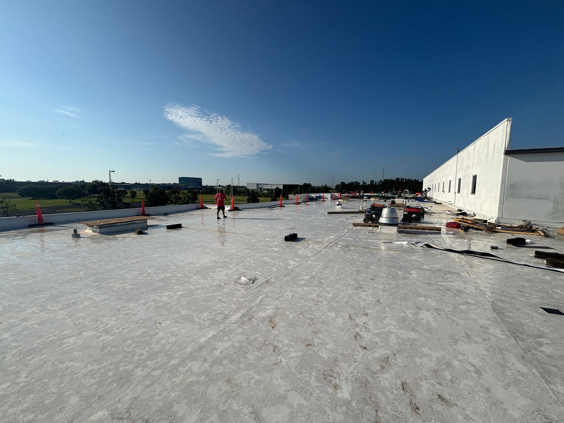 A person on a white roof under a blue sky, construction materials scattered about.