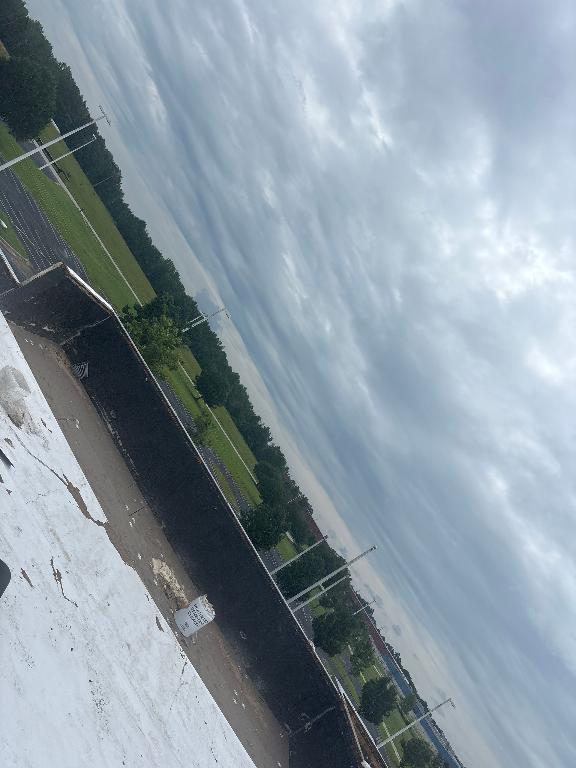 Overcast sky above a green park, seen from a building rooftop with white and black surfaces.