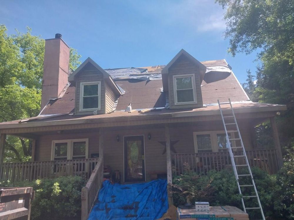 House with roof partially torn off; ladder leaning against side. Blue tarp covers porch.