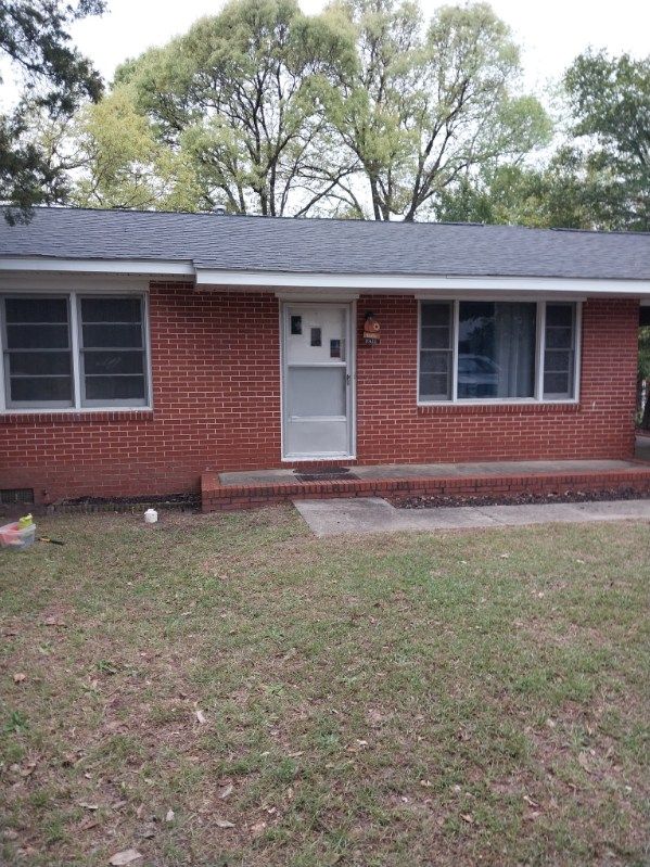 Red brick house with a gray roof and white door, flanked by windows. Lawn in front.