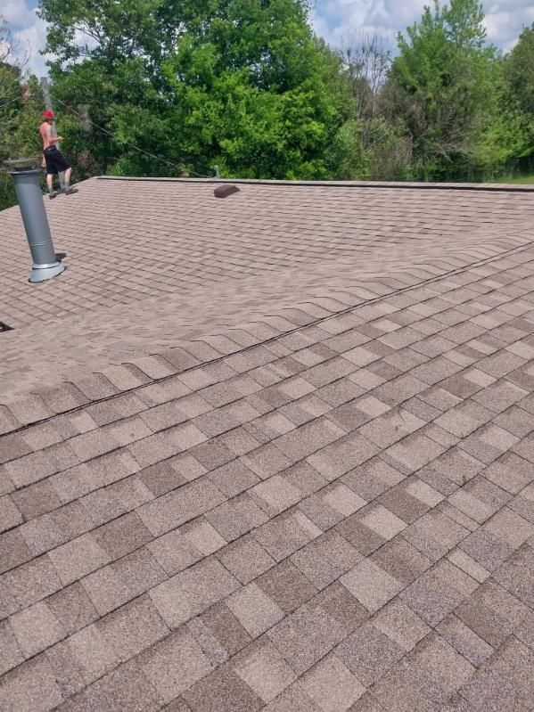 Roof with brown shingles, person standing, trees in the background.