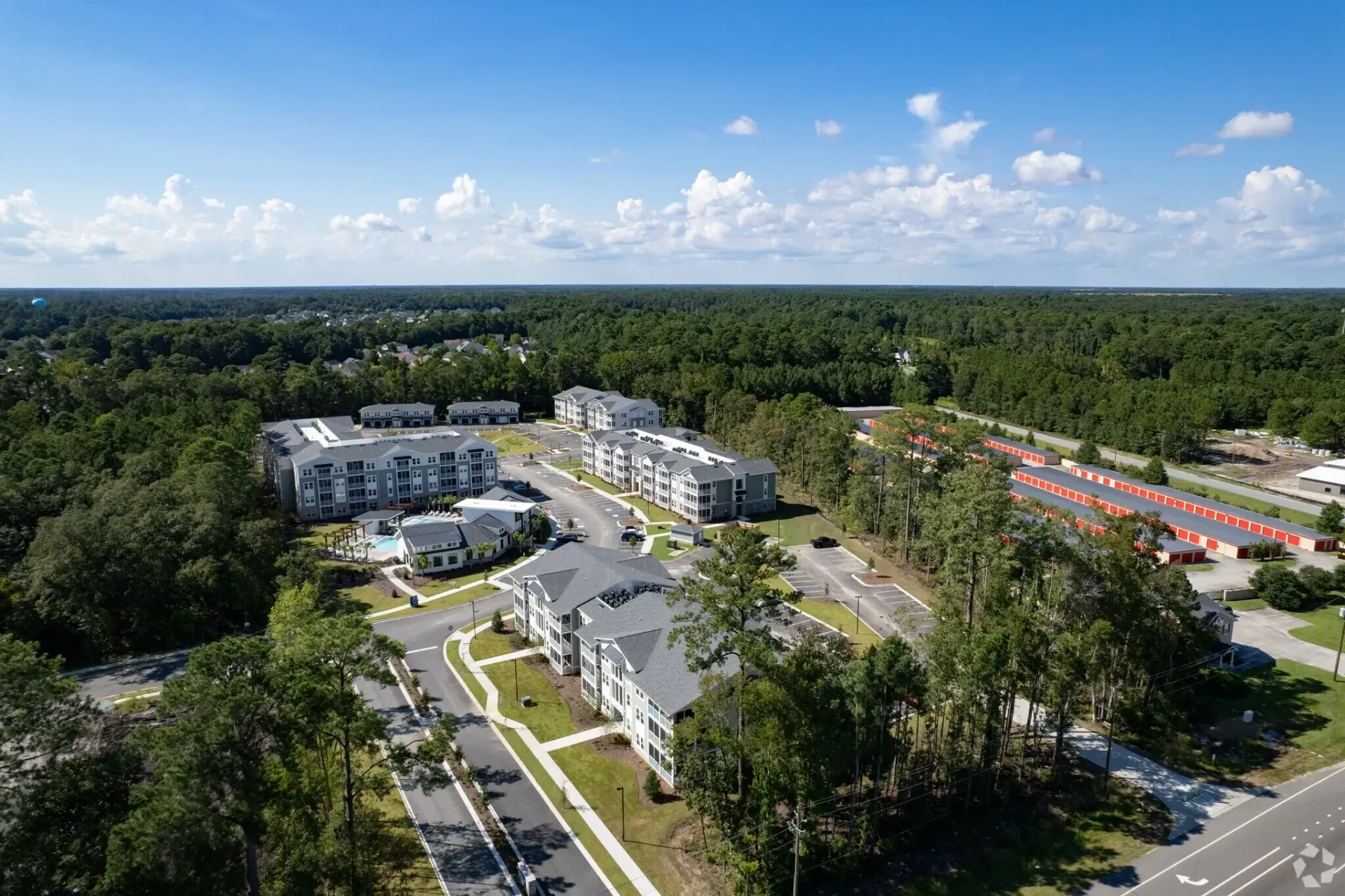 Aerial view of apartment complex buildings, a swimming pool, and surrounding landscape with storage units.
