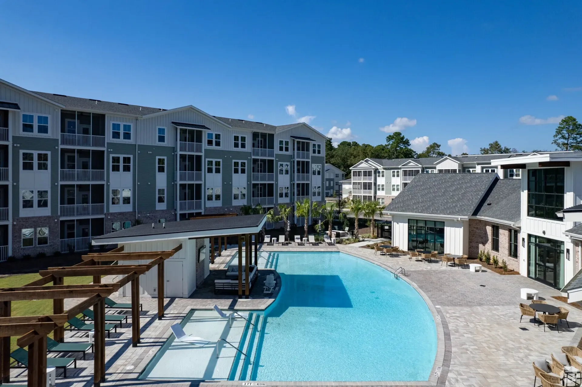 Modern apartment complex courtyard with a large, bright blue swimming pool and lounge chairs.