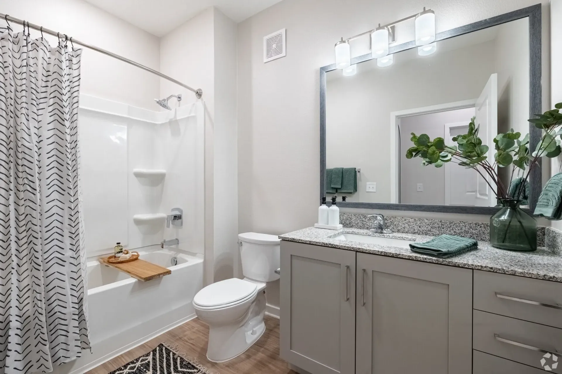 Bright modern bathroom with white shower curtain, vanity, large mirror, and gray cabinets