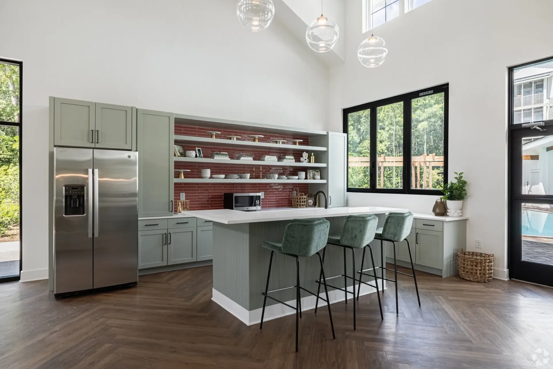 Modern kitchen with island, bar stools, stainless steel refrigerator, and poolside view.