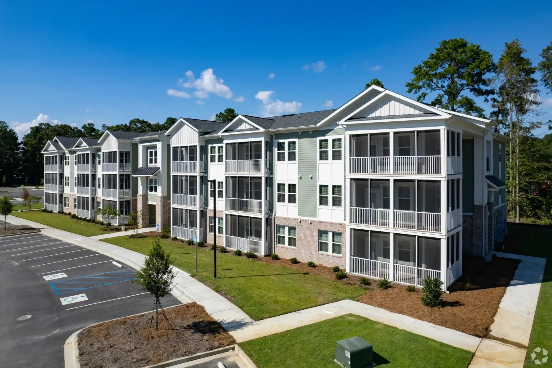 Exterior view of a multi-story apartment building with screened-in balconies and a parking lot.