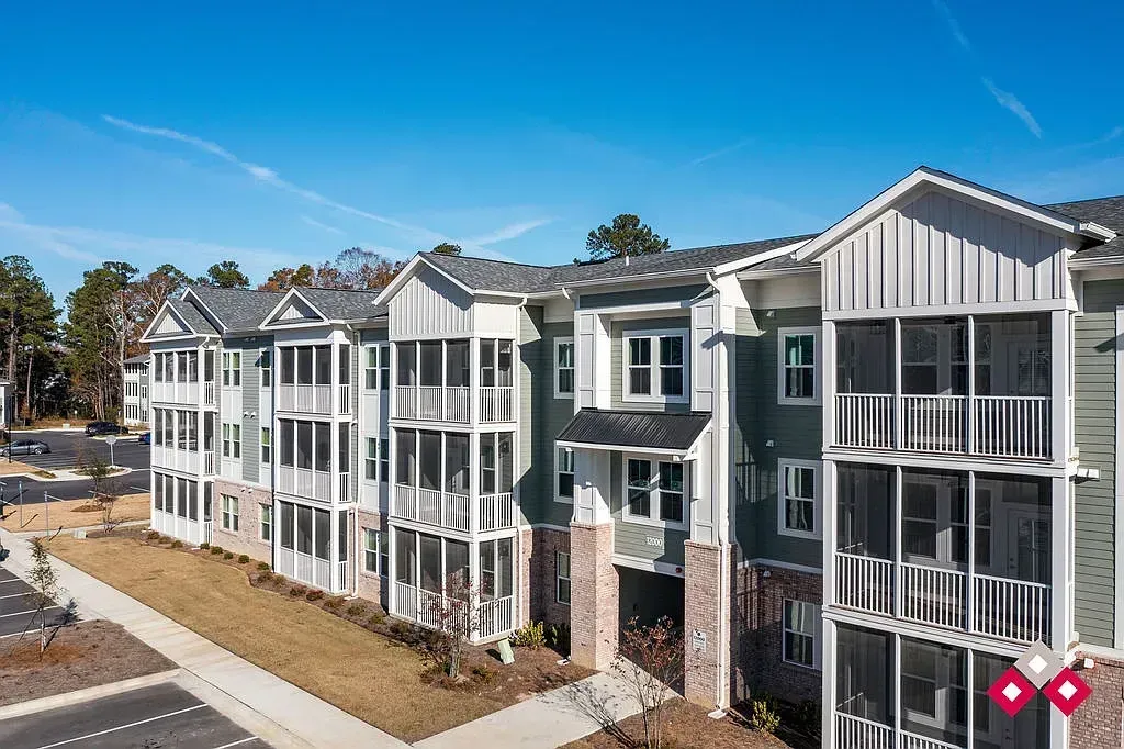 Exterior of a multi-story apartment building with green siding and white trim, featuring balconies with white railings and screened-in porches.