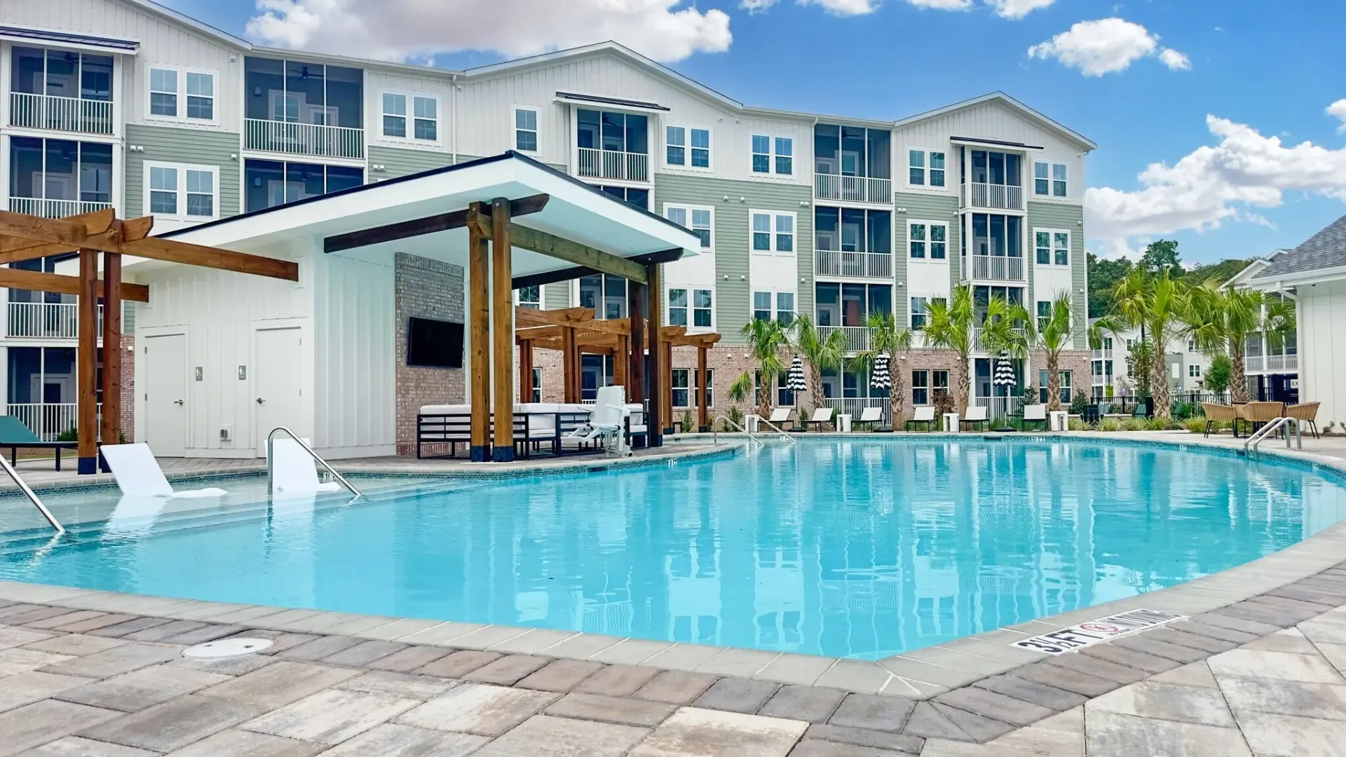 Outdoor swimming pool with a cabana and lounge chairs next to a multifamily apartment building.