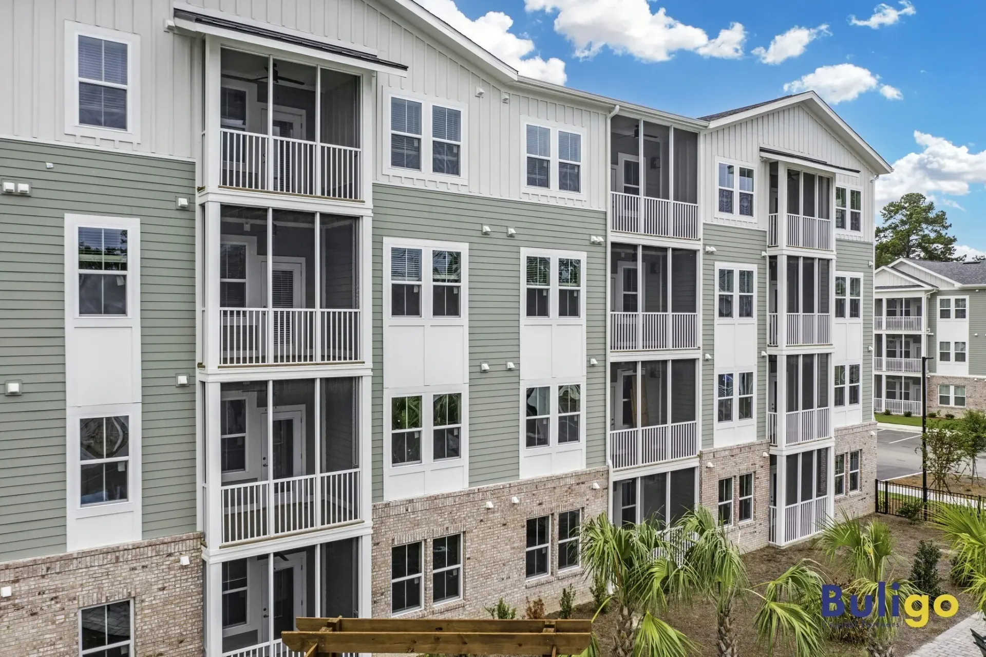 Exterior view of a multi-story apartment building with green siding and white balconies.