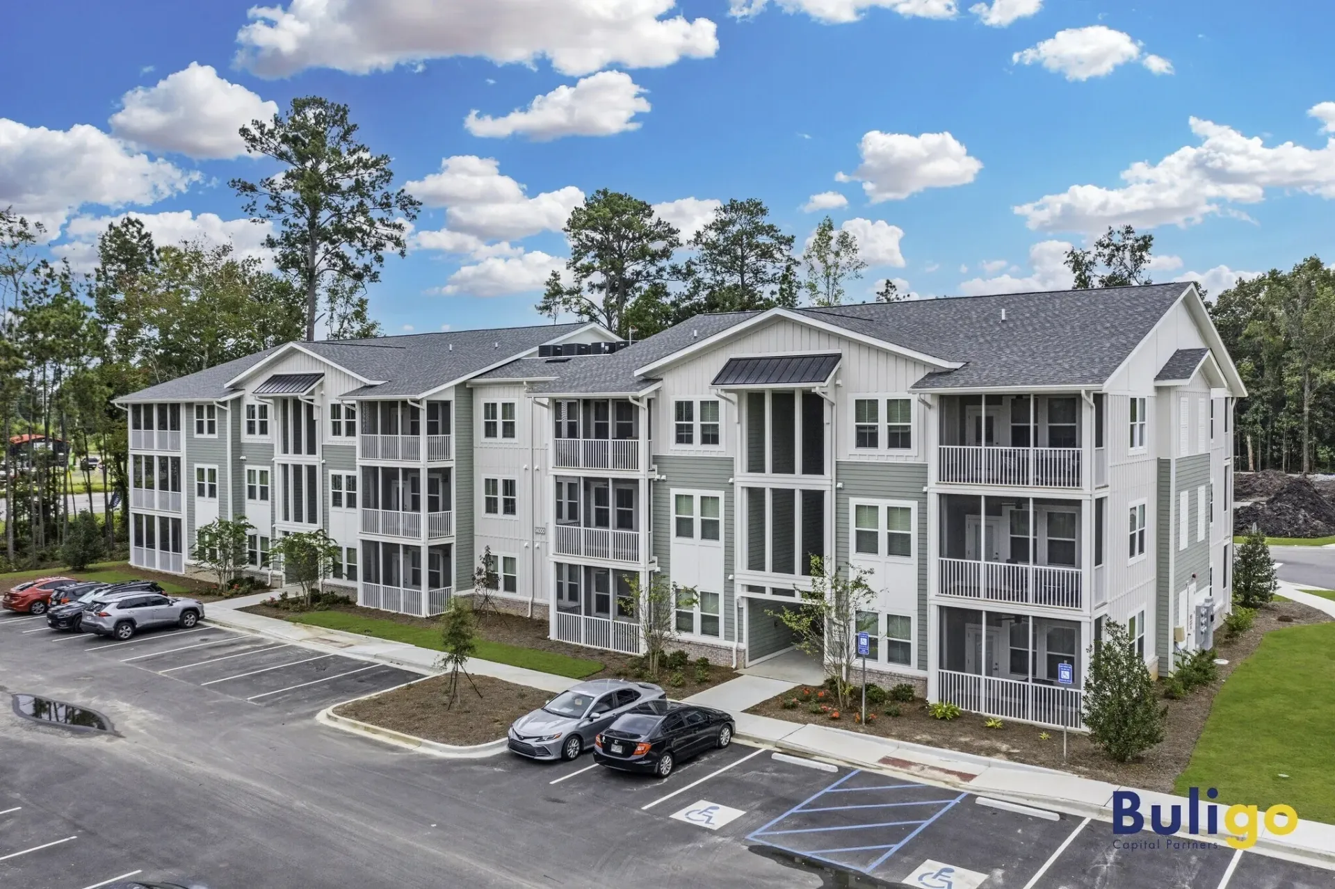 Exterior view of a multi-story apartment building with parking lot and green landscaping.