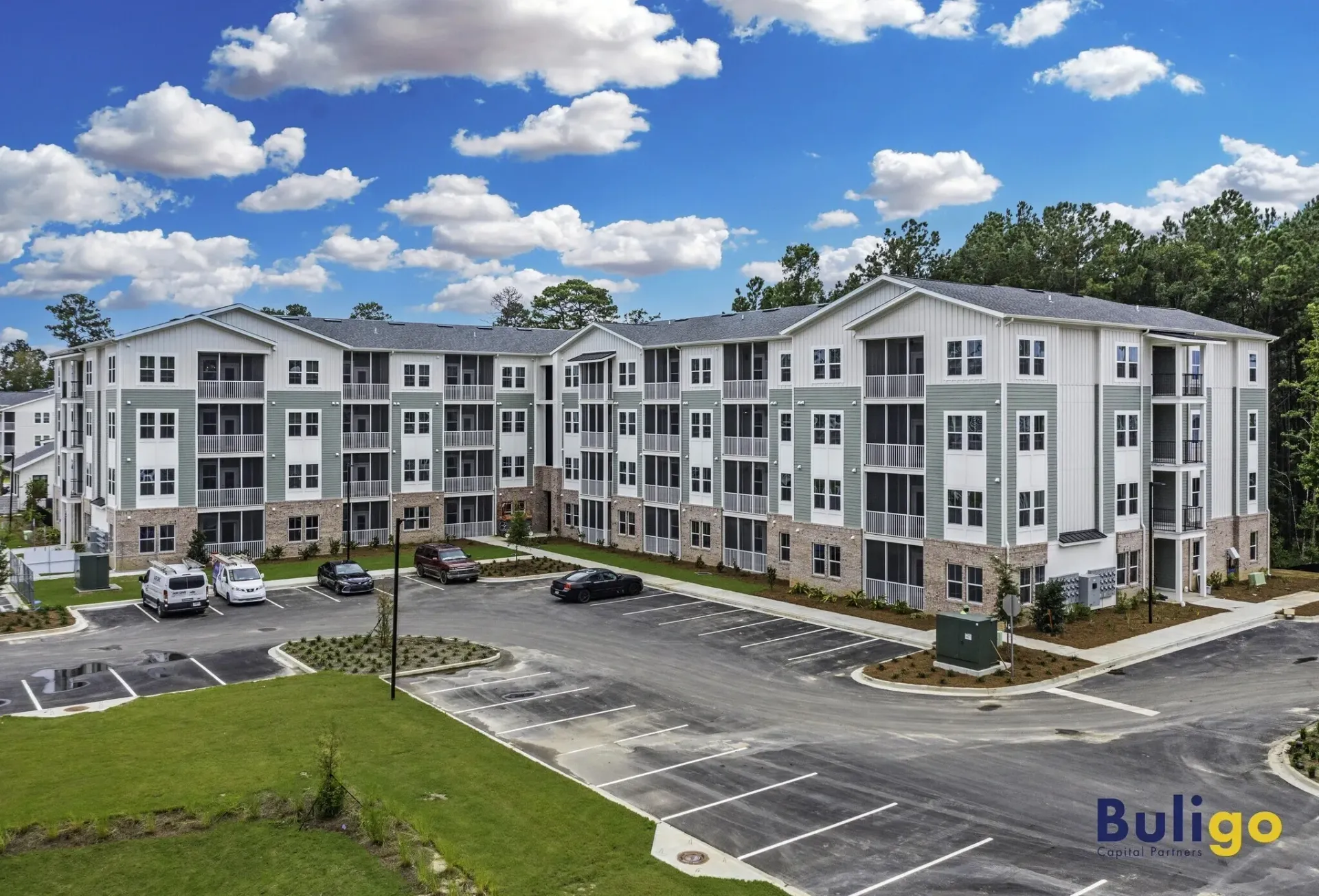 Exterior of a modern apartment building with balconies and a parking lot.
