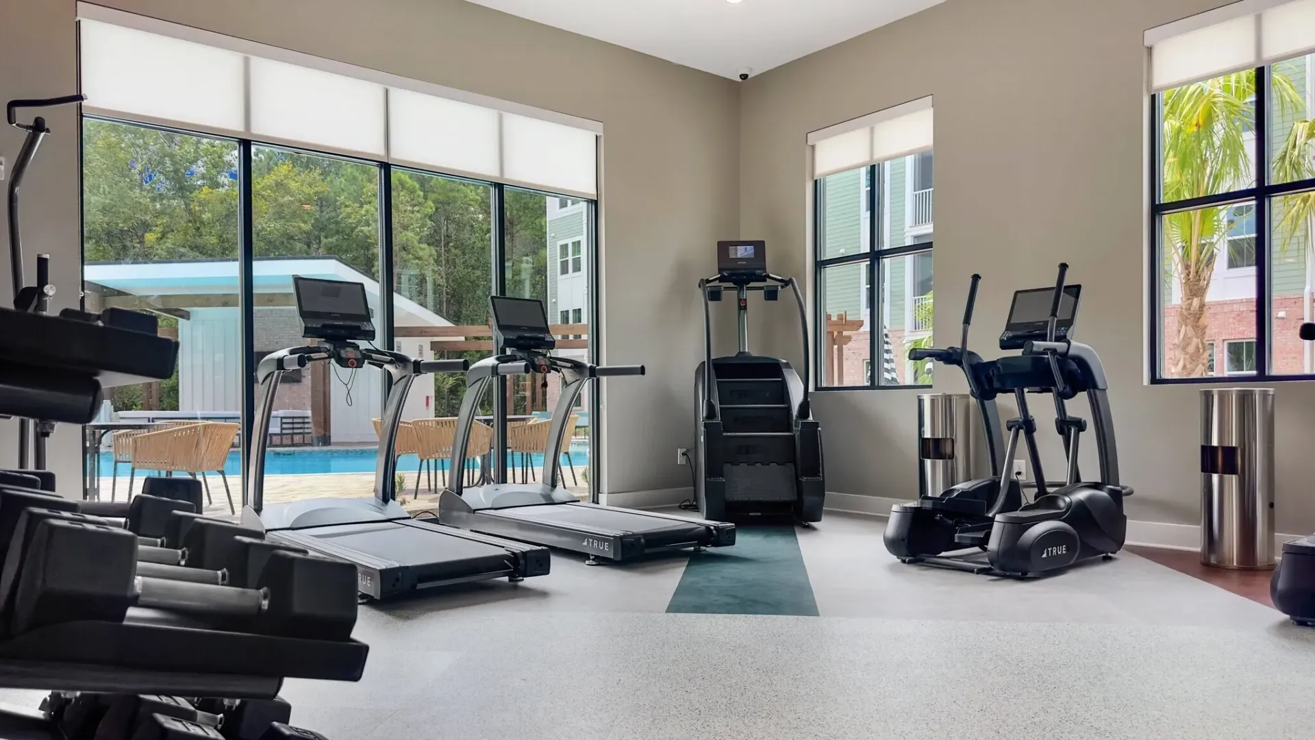 Fitness center with treadmills, ellipticals, and dumbbells, overlooking an outdoor pool.