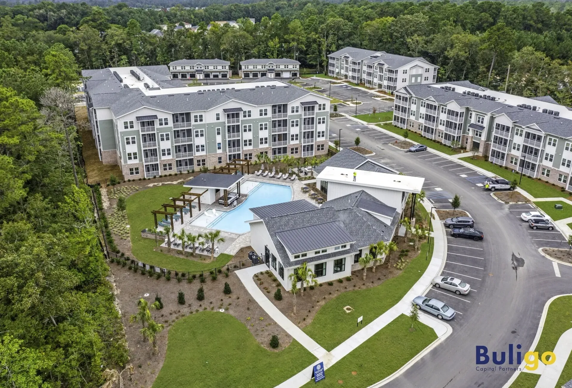 Aerial view of a modern apartment complex featuring a swimming pool, clubhouse, and ample parking.
