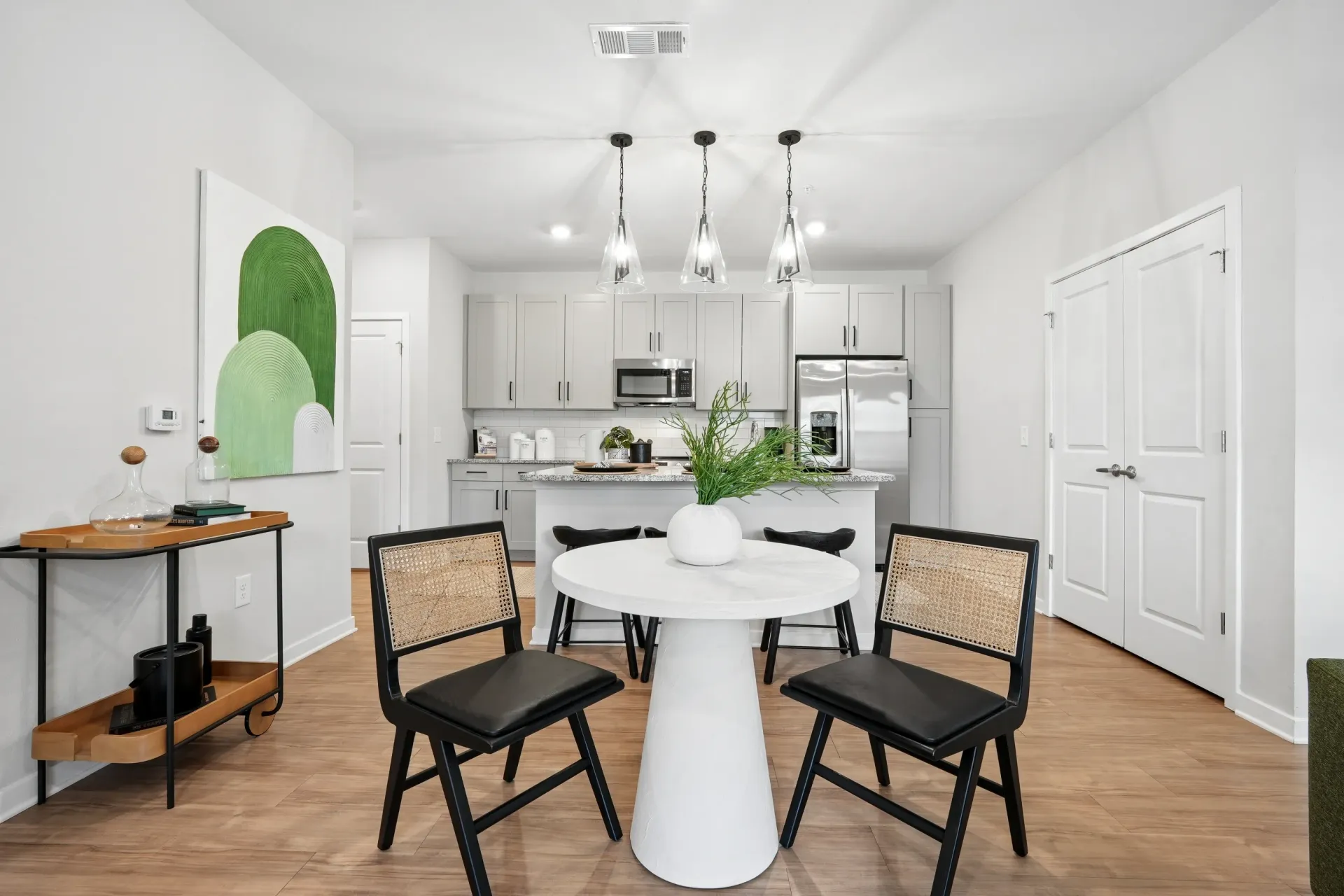 Modern dining area and kitchen in an apartment with light gray cabinets and stainless steel appliances.