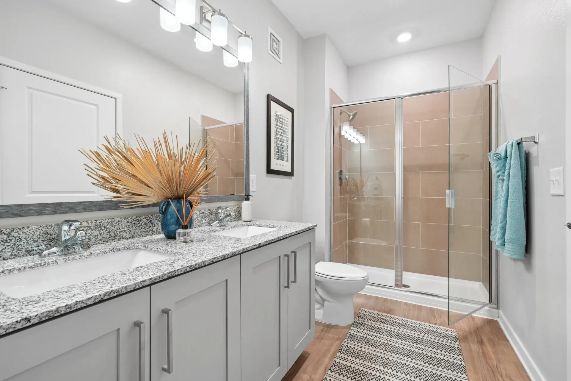 Modern bathroom with double vanity, granite countertops, and a glass-enclosed shower.