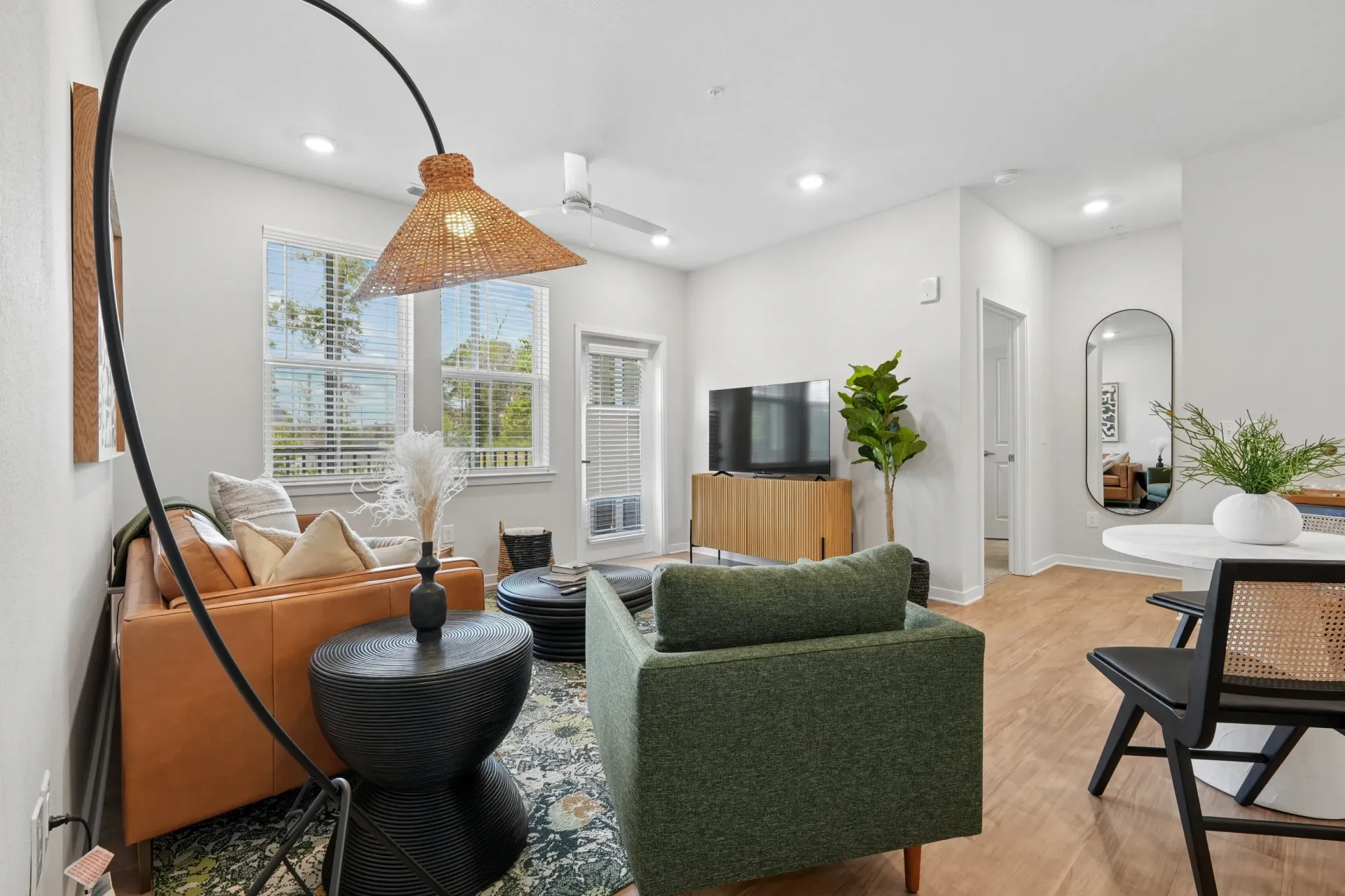 Modern living room with leather sofa, green armchair, TV on media console, and dining area.