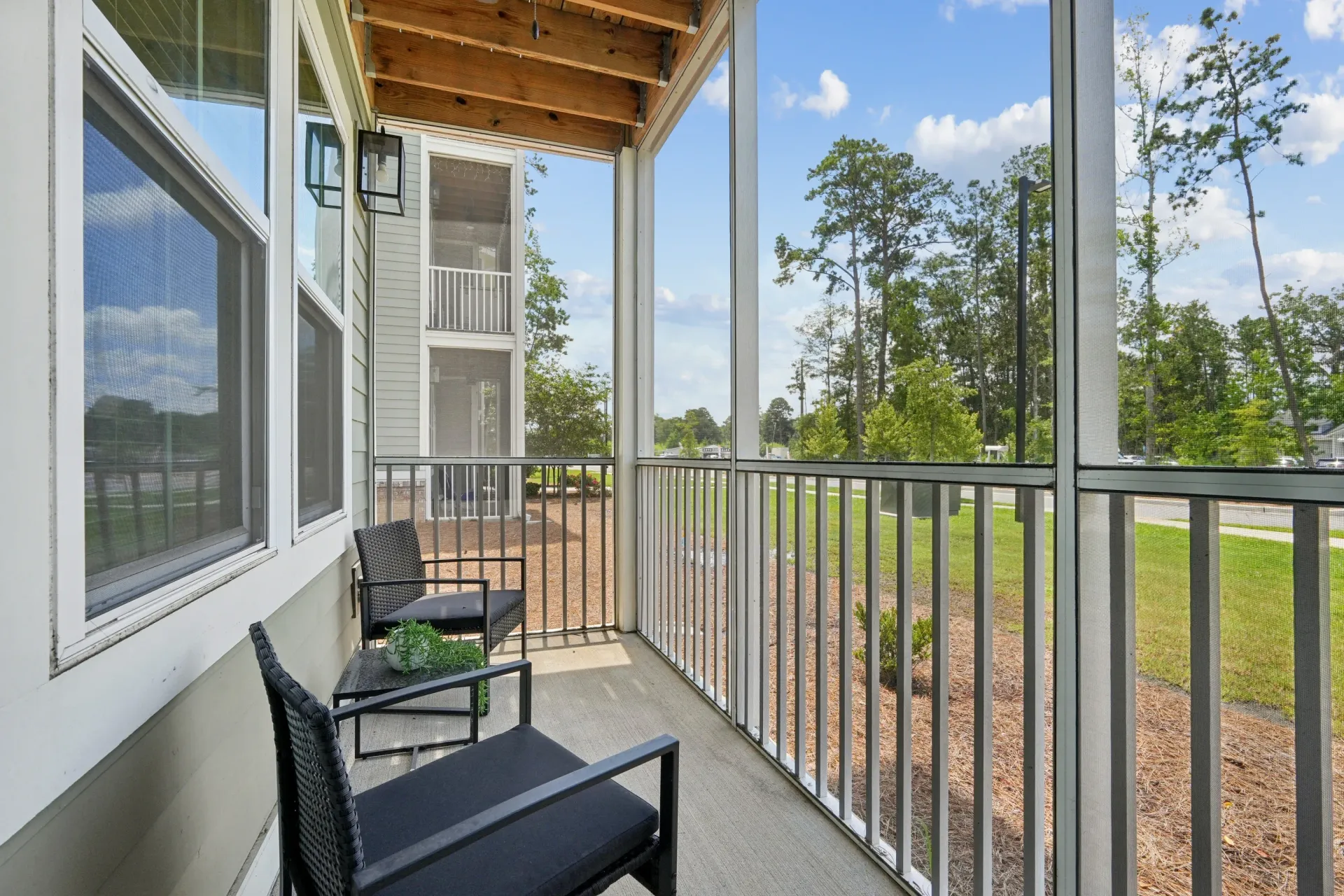 Screened-in balcony with seating and view of trees and building exterior.