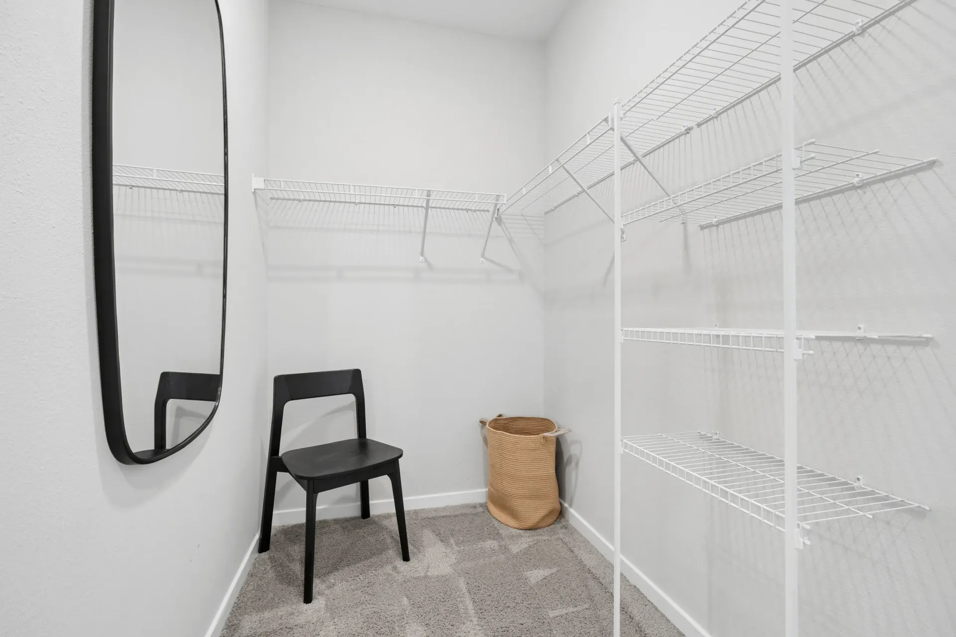 Empty walk-in closet with white wire shelving, a black chair, and a woven basket.