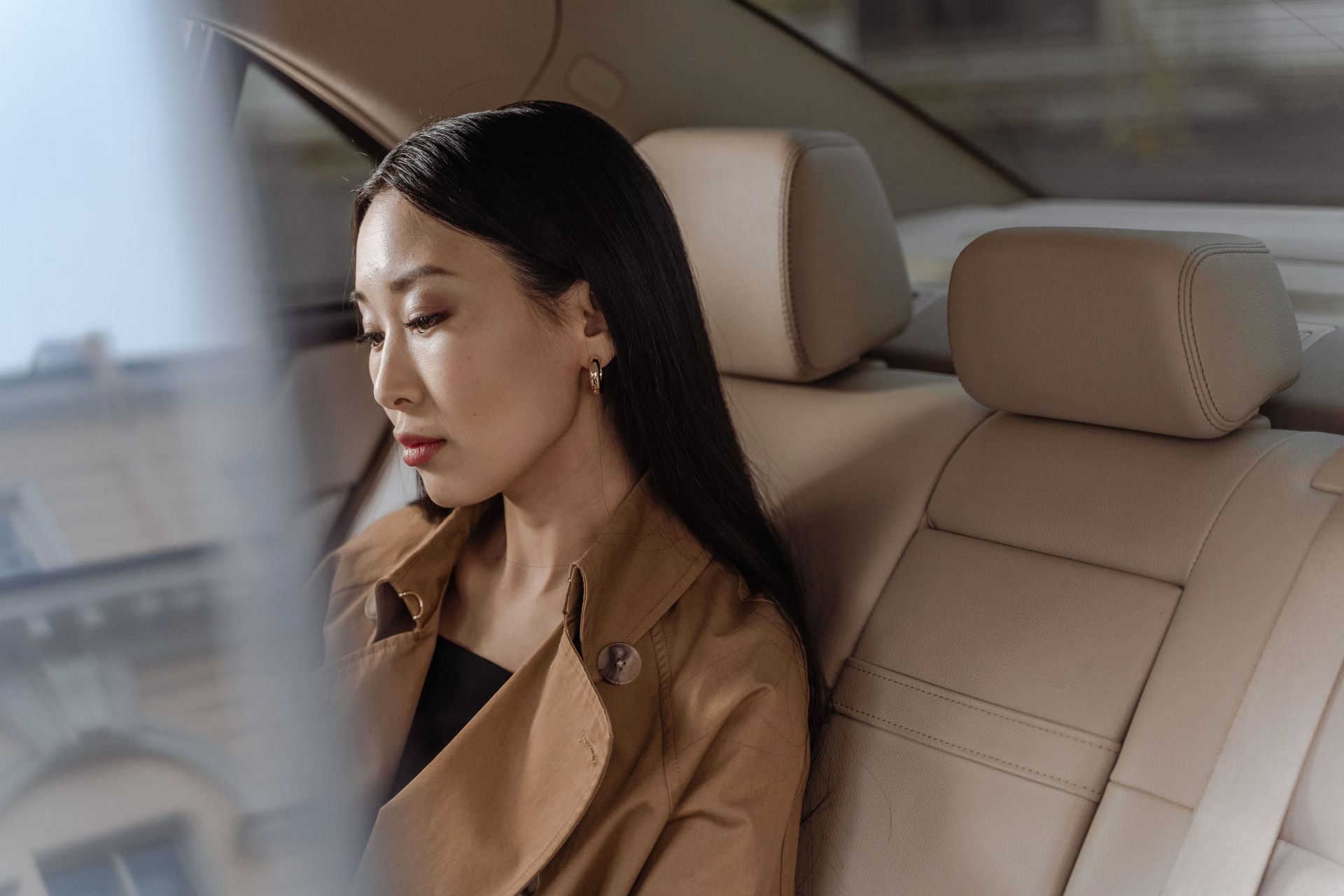 Woman in a tan coat sitting in the back seat of a car, looking out the window