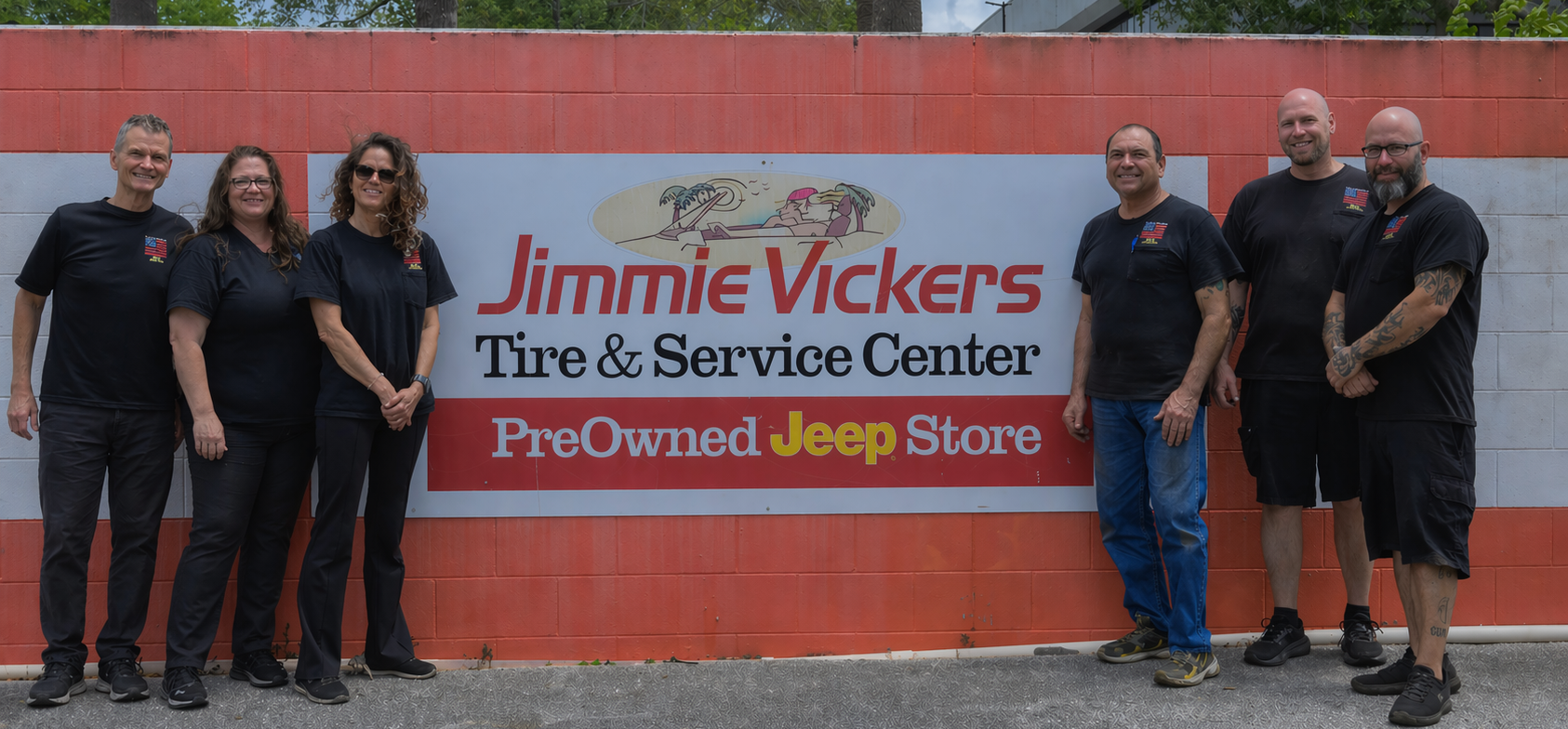 Group of six standing by a Jimmie Vickers Tire & Service Center PreOwned Jeep Store sign