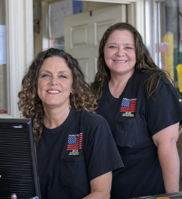Two smiling coworkers in black T-shirts standing indoors near a counter and doorway