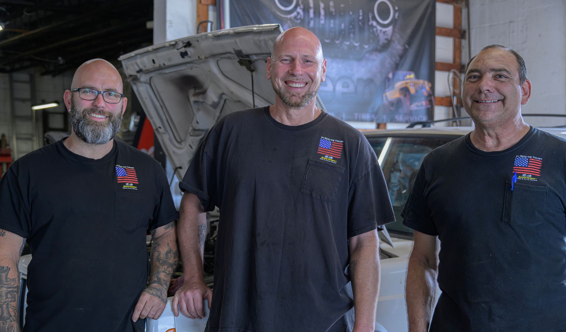 Three smiling men in black shirts standing in front of an aircraft in a hangar