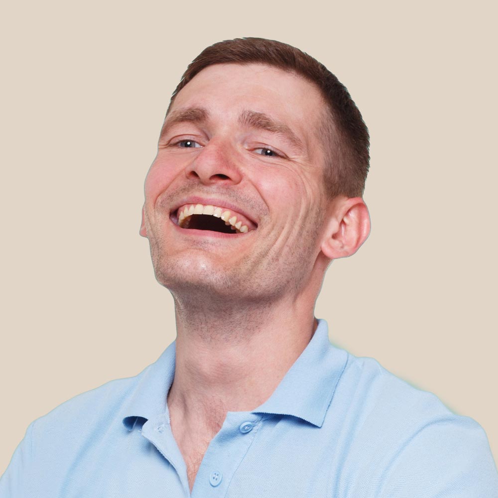 Man with short brown hair wearing a light blue polo shirt, laughing with his mouth open.