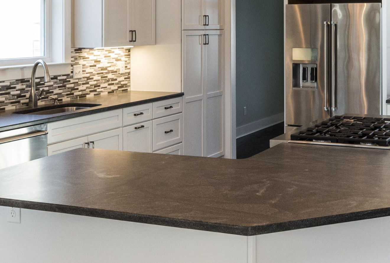 A modern kitchen featuring white cabinets, a dark countertop, stainless steel appliances, and a tile backsplash.